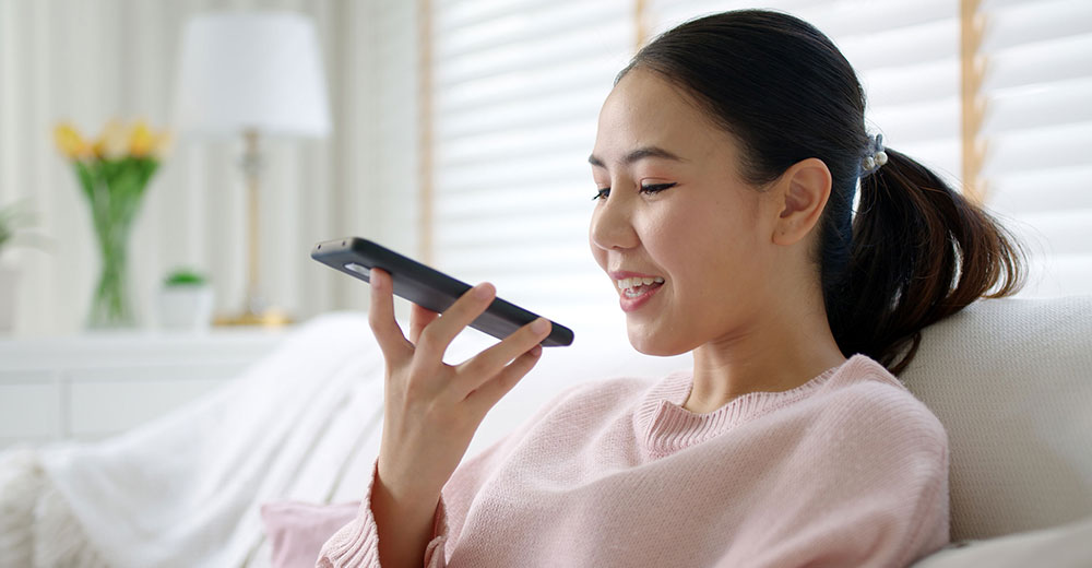 Woman speaking into smartphone while using a voice-based AI assistant.